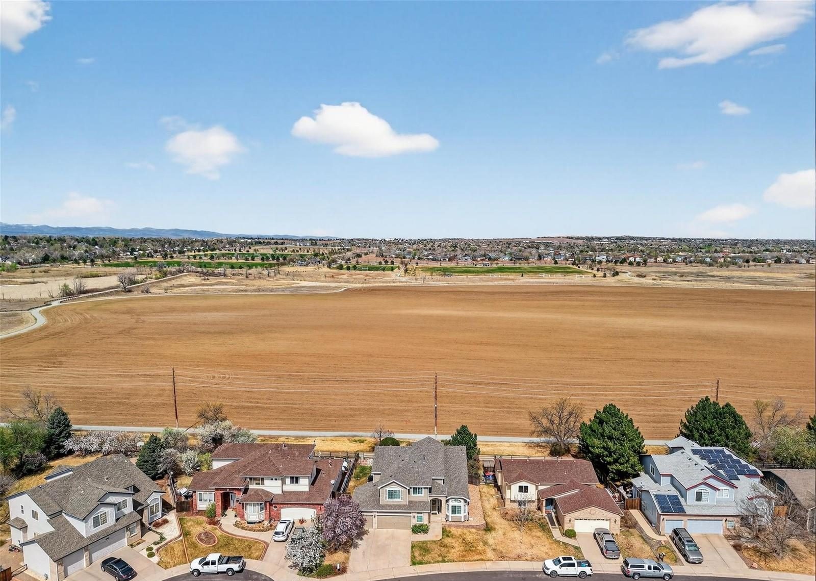Aerial view over a Broomfield neighborhood and open fields, with the Front Range on the horizon.