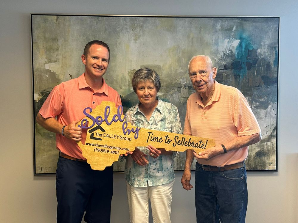 Steve Calley with an older couple holding the Sold by The Calley Group key sign at closing.