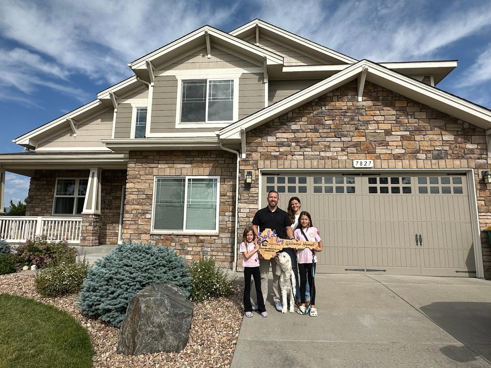 A family with two daughters and a dog in front of a stone-front home, holding the Calley Group key sign.