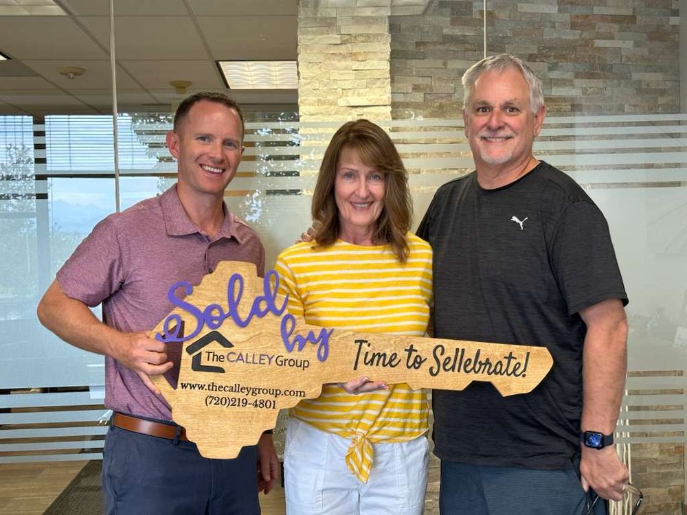 Steve Calley with a couple holding the Time to Sellebrate key sign in an office.