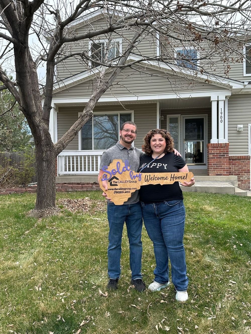 A couple holding the Welcome Home key sign on the lawn of their new home.