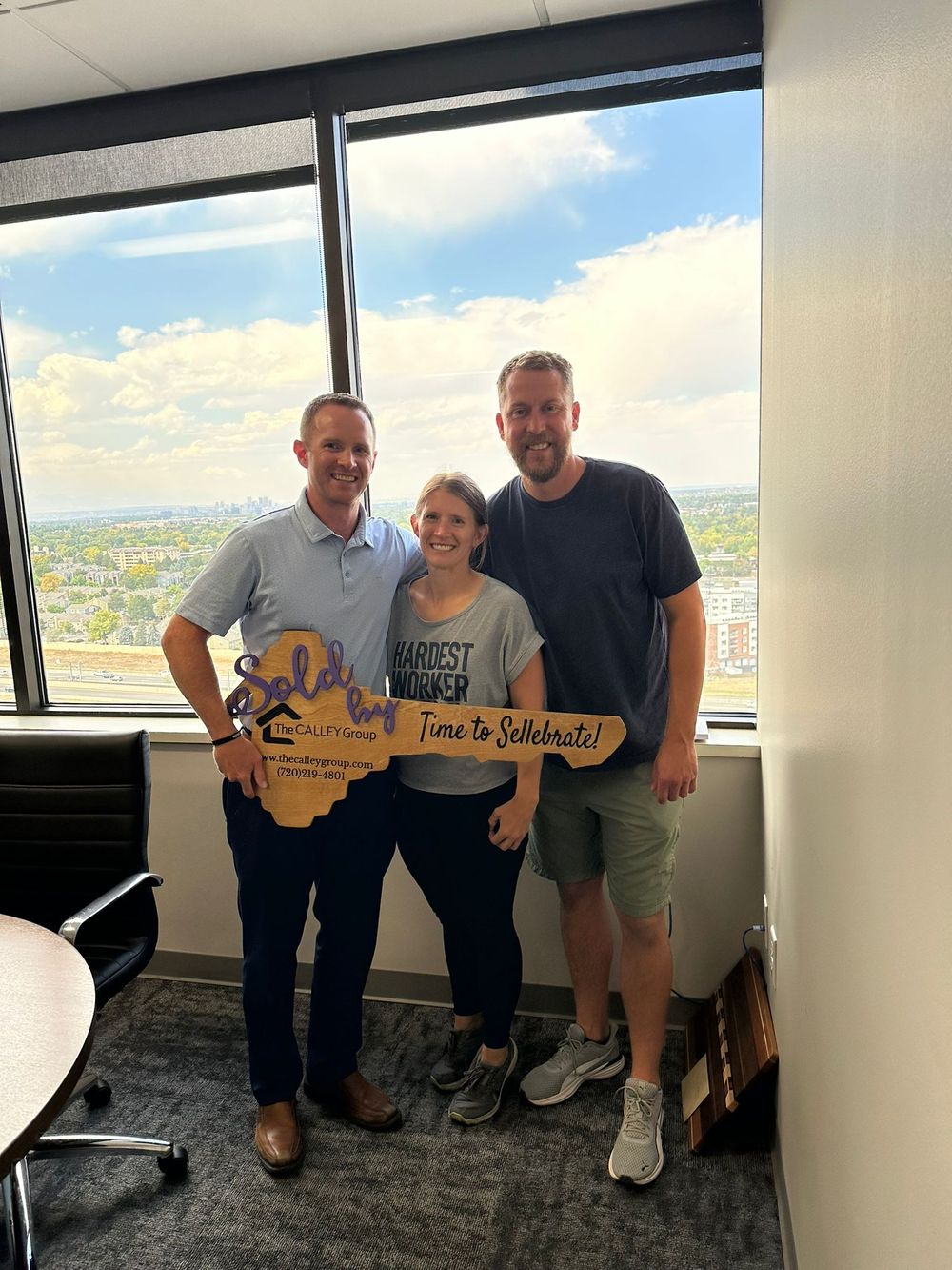 Steve Calley with a couple holding the Time to Sellebrate key sign by an office window.