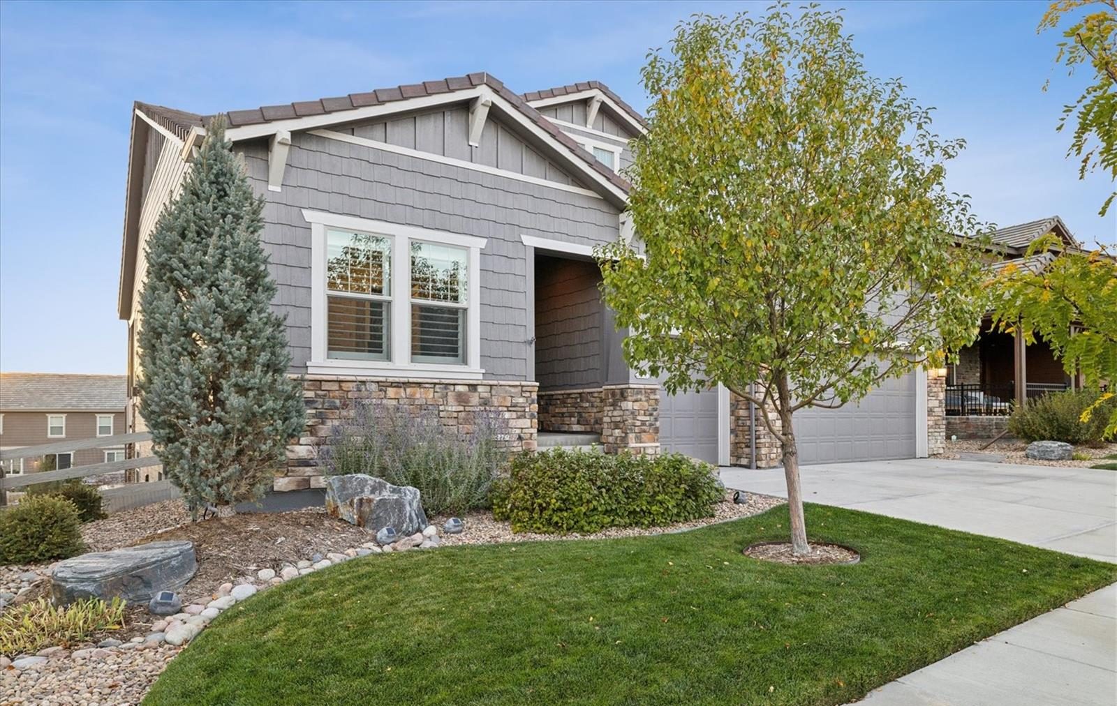 Gray craftsman home with stone accents and a young tree.