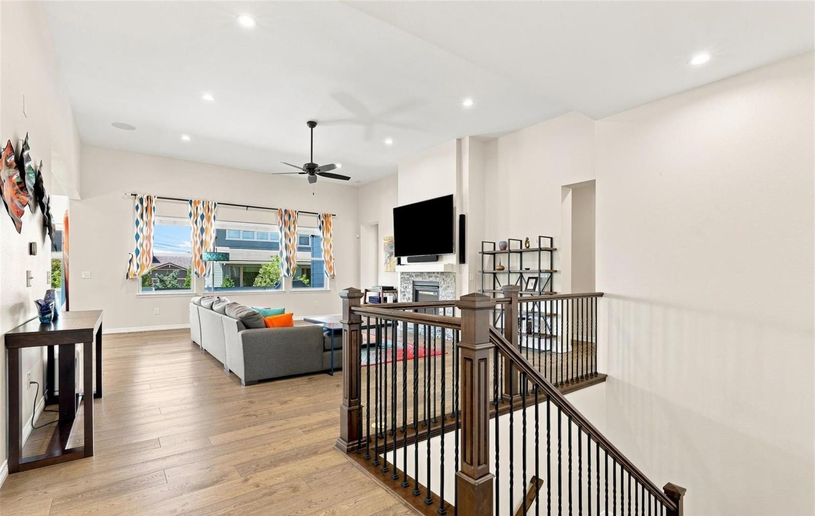 Open living room with a fireplace and a wall-mounted TV, beside a railed staircase to the lower level.
