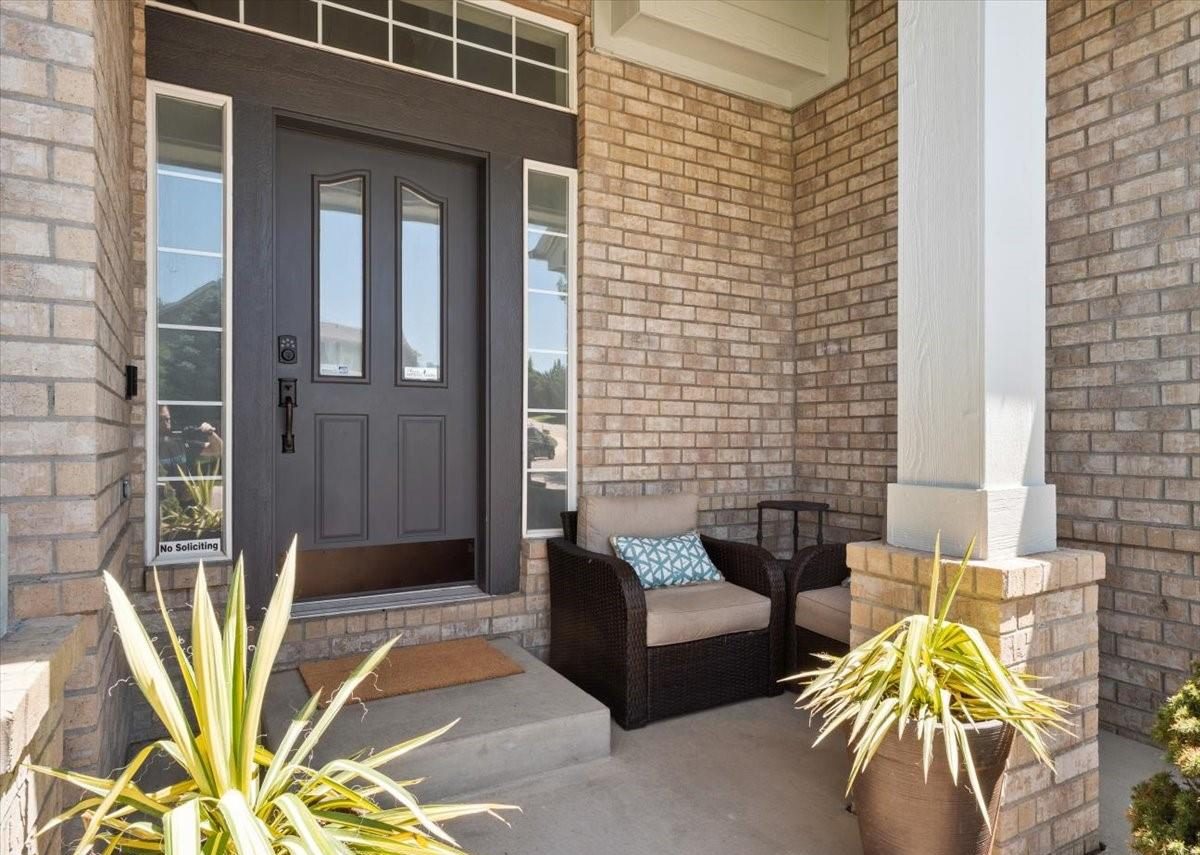 Covered front entry of a brick home with a dark front door and potted plants.