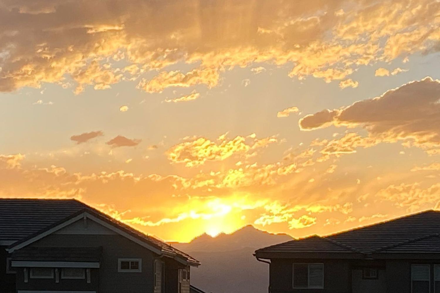 The sun setting behind the mountains between two Anthem Highlands rooftops.
