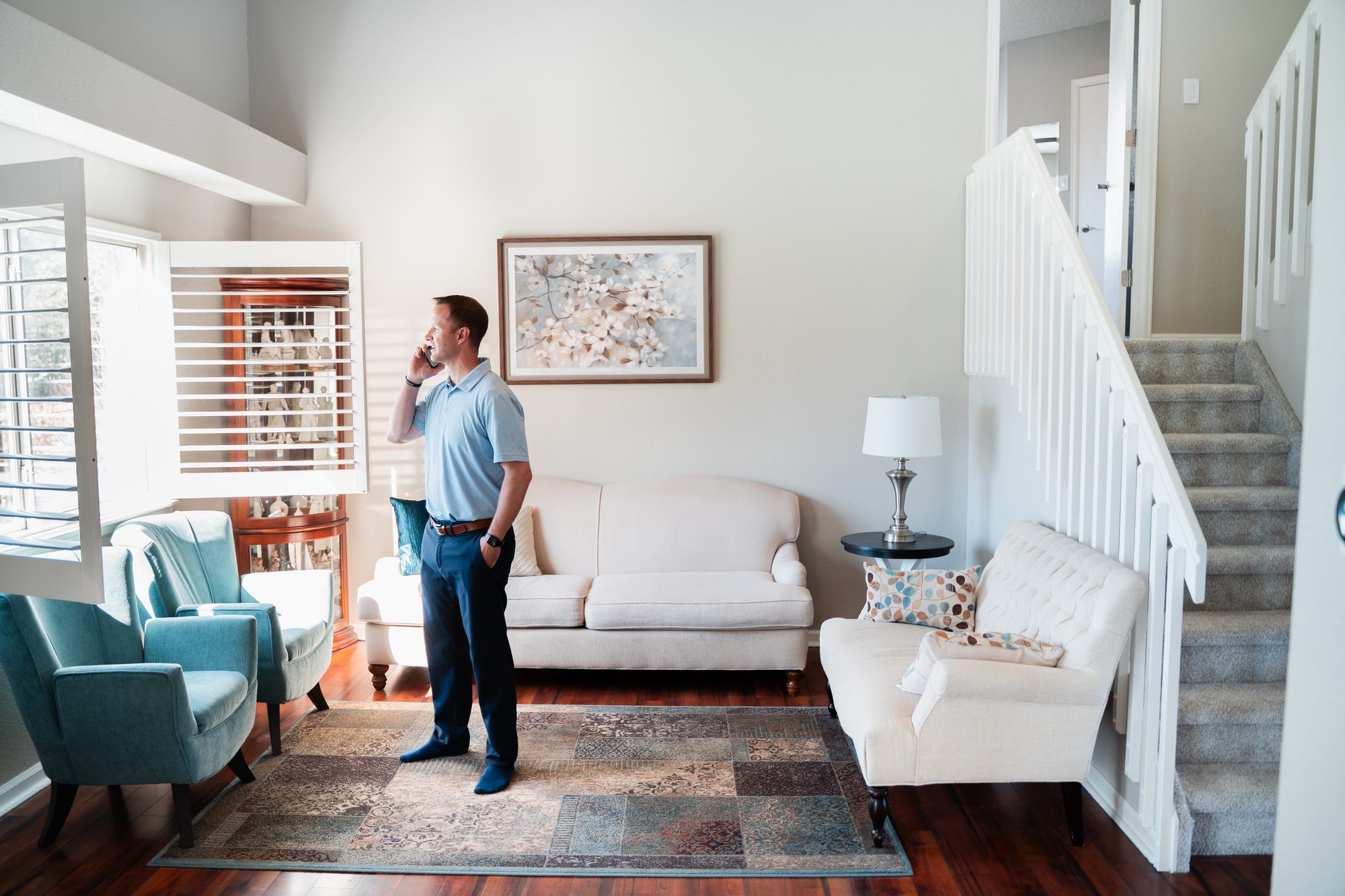Steve Calley on a phone call in a bright living room with a white staircase.