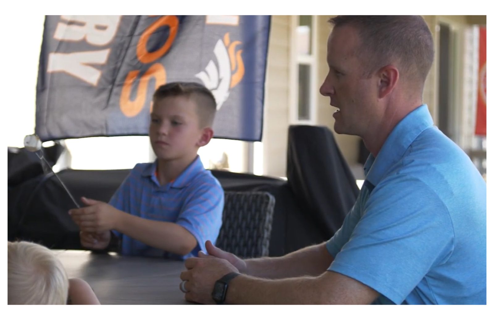 Steve Calley sitting at a table with his young son, a Broncos flag in the background.