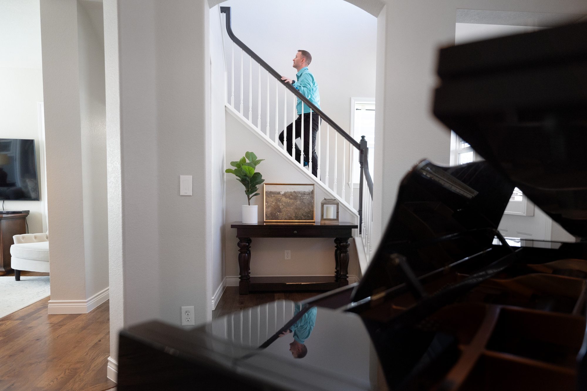Steve Calley walking up the staircase of a home, seen past a grand piano.