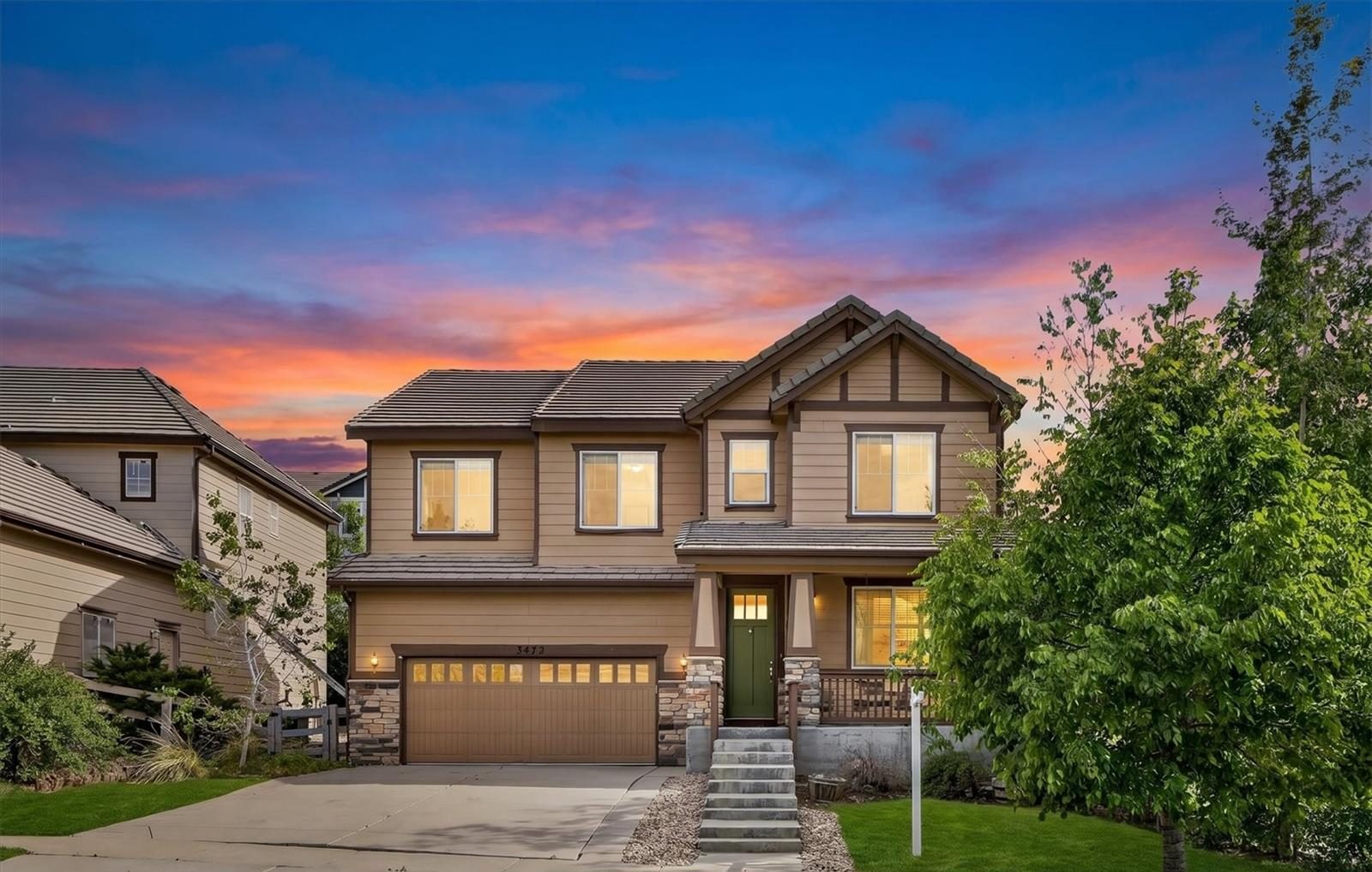 Two-story craftsman home in Broomfield at twilight, with lights on inside and a pink and blue sky.